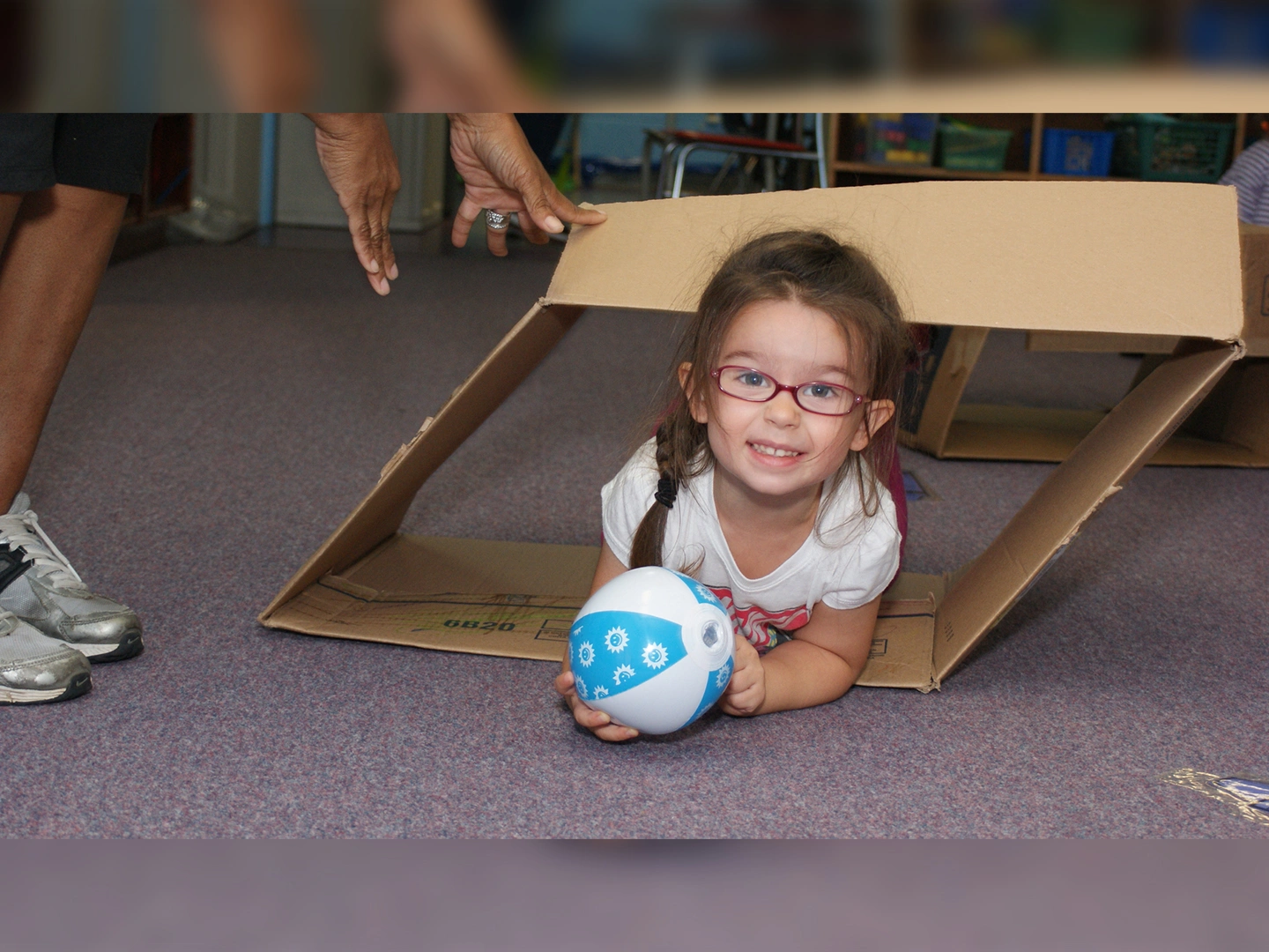 A little girl laying on the floor holding a ball.