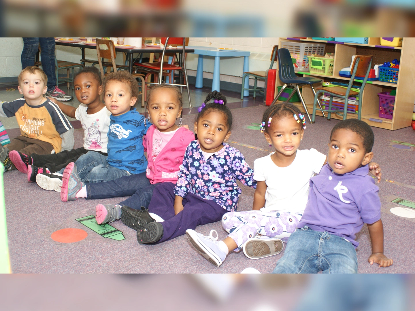 A group of children sitting on the floor in front of some books.