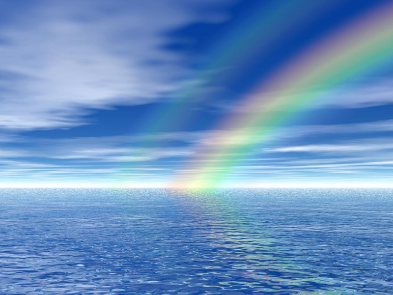 A rainbow is seen in the sky over water.